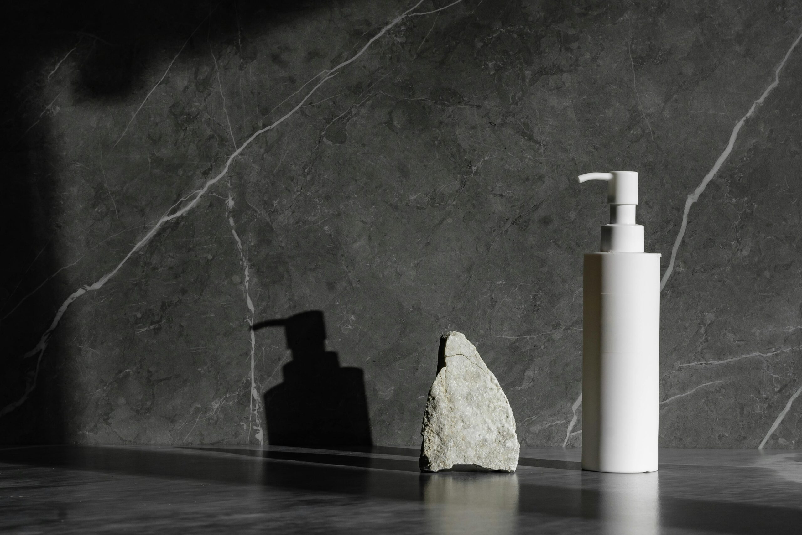 Sleek white pump bottle beside a rock on a marble surface with dramatic lighting.